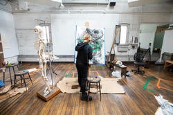 risd student in a brightly lit classroom facing their drawing next to a skeletal model